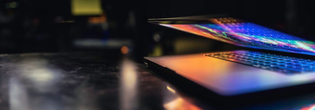 a laptop half closed in the dark with colorful glow.